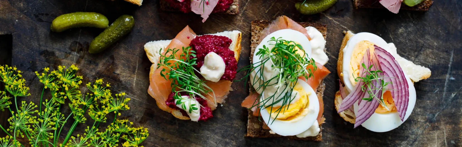 Smörrebröd med lax, ägg, rödbetsröra och rödlök på träbräda med dill och gurka