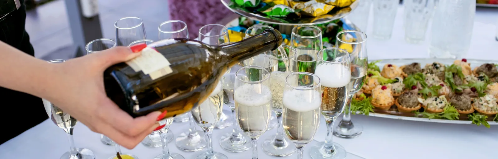 Champagne hälls upp i glas vid buffé med små pajer