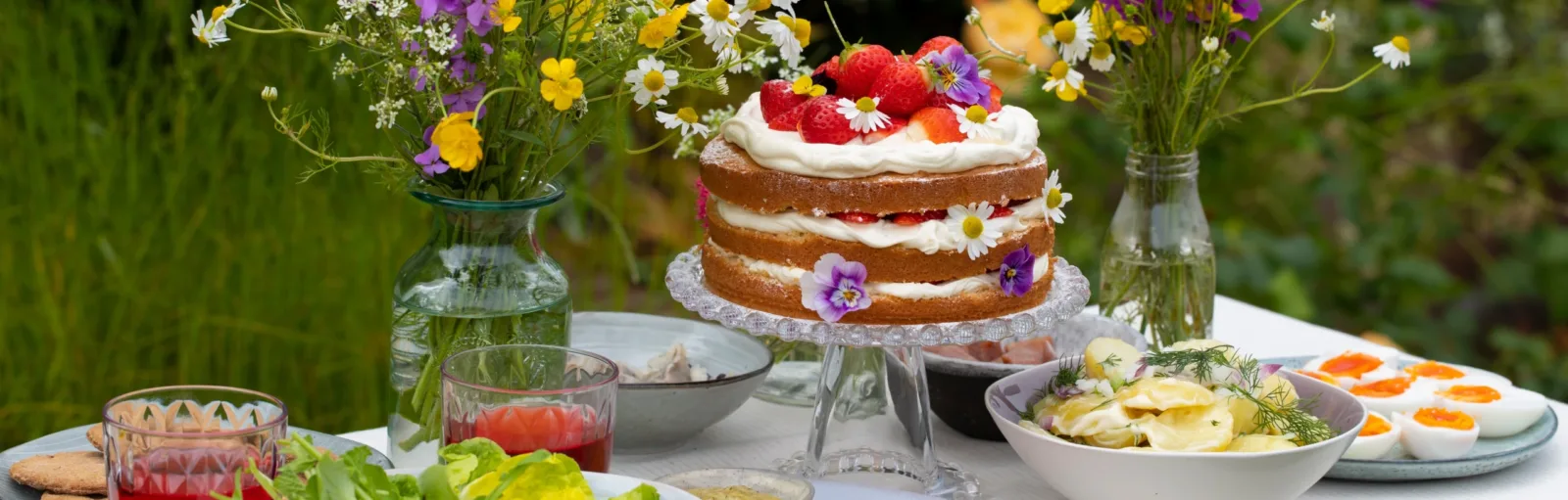 Midsommarbord med jordgubbstårta, blomsterbukett, sill och ägghalvor